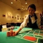 an asian dealer leaning over a casino table