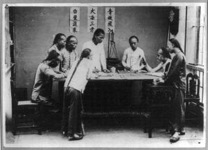 a couple of young men playing fan tan in acient asia, circled around a table